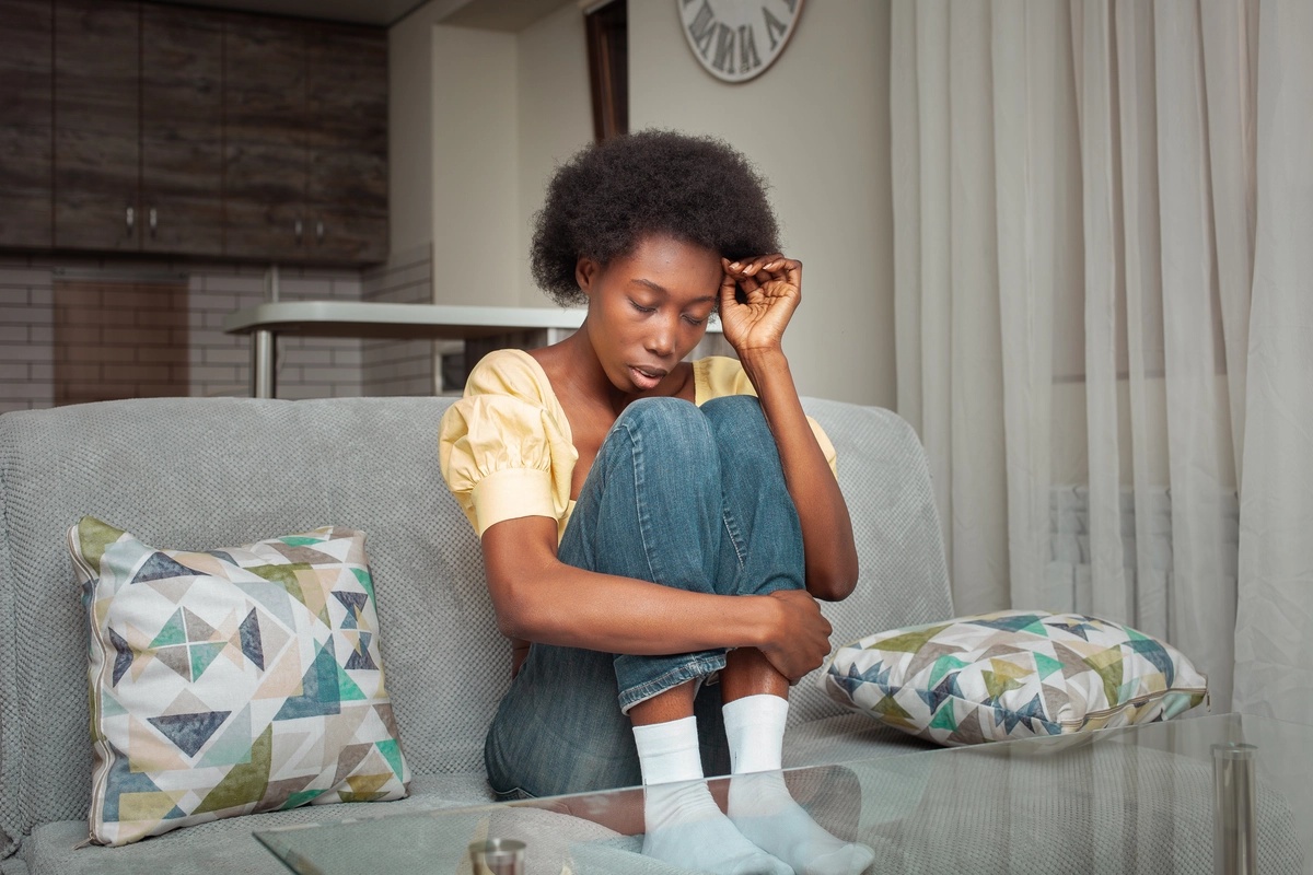 A woman sitting on a couch with her knees to her chest, struggling with withdrawal and considering detox.