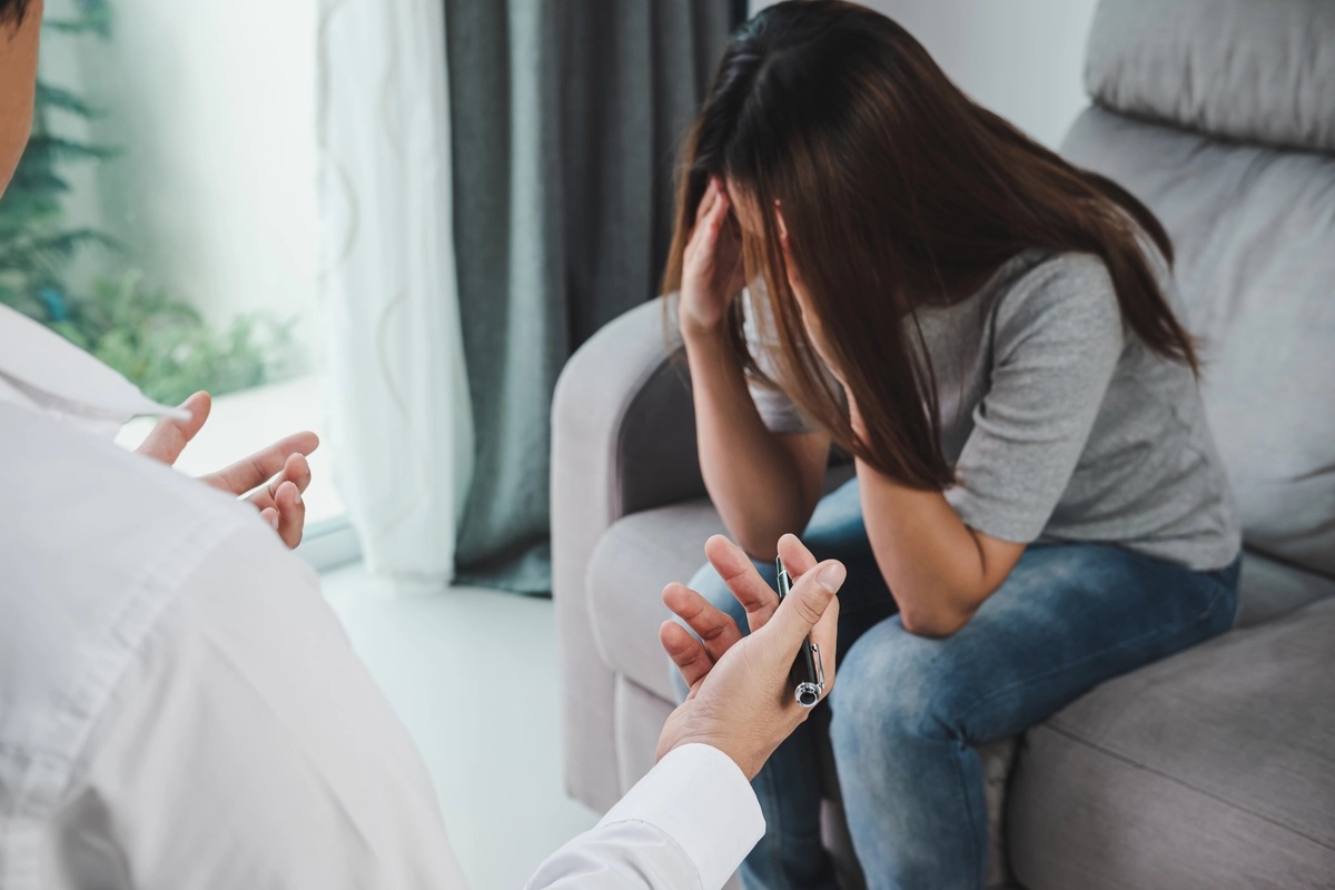 A woman in a chair with her hands to her face. A doctor is speaking to her.