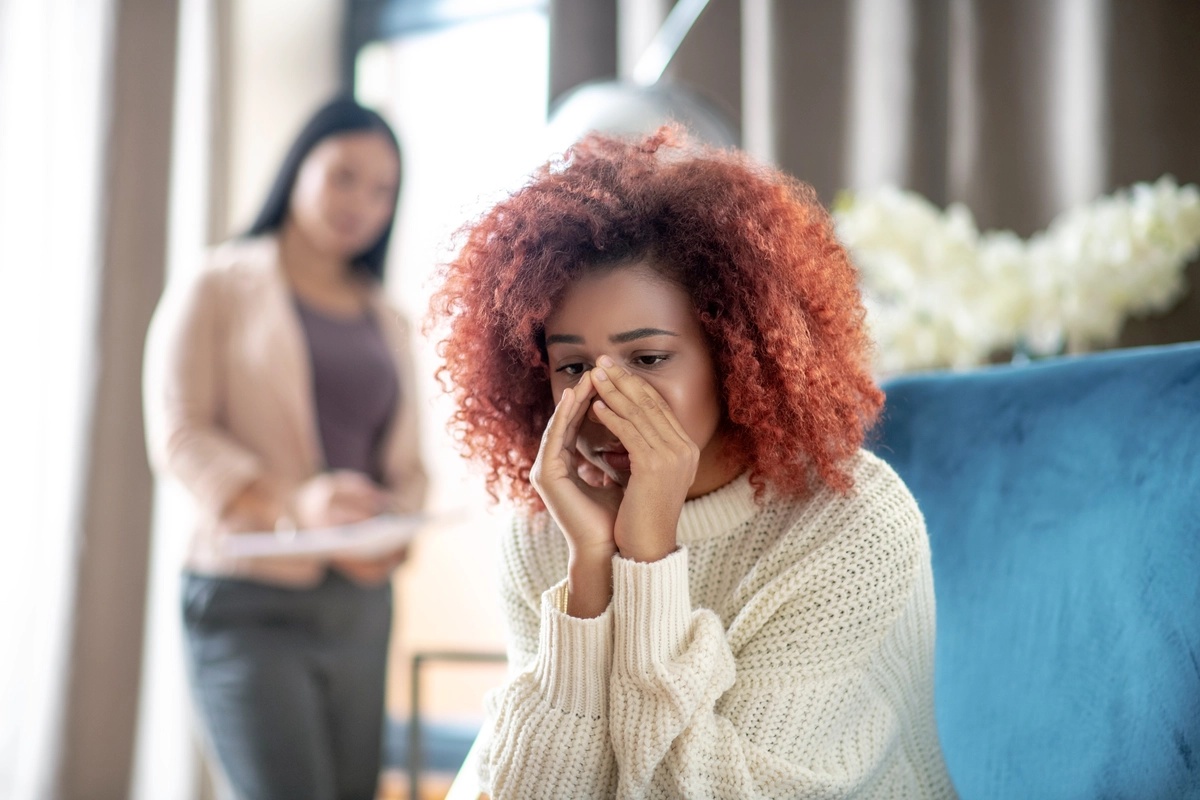 A woman sits on a couch with her hands to her nose.