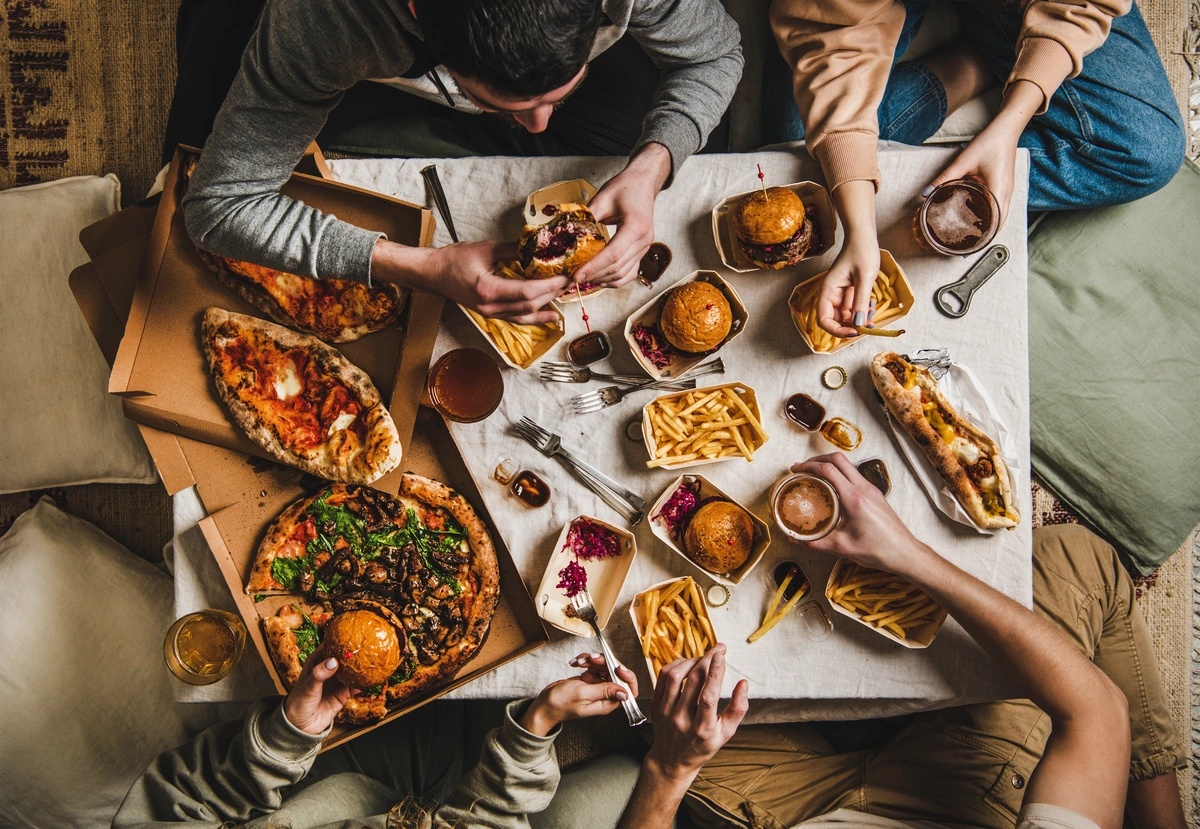 A group of people sitting around a table with large portions of food, representing the gluttony food addiction causes.