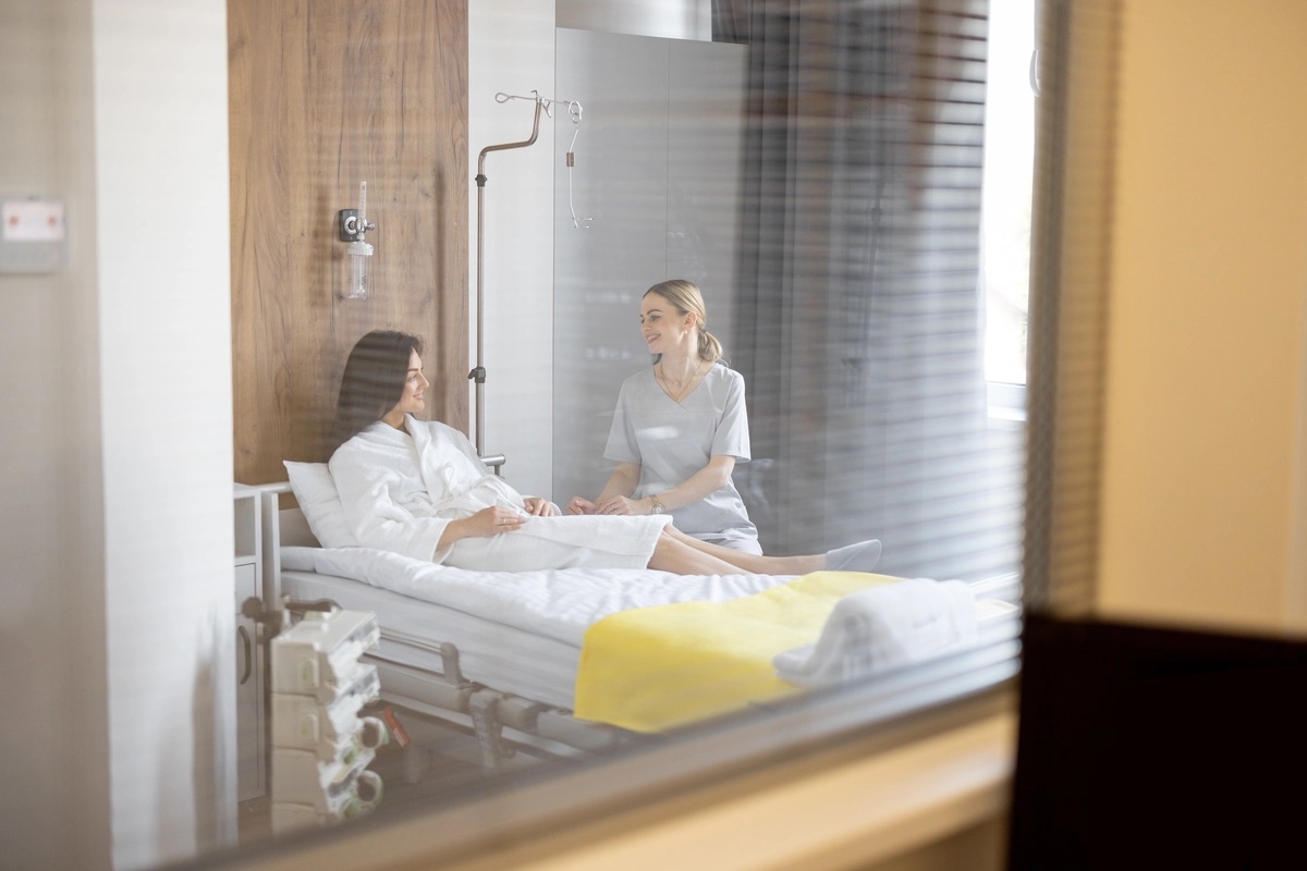 A woman laying on a hospital bed while in inpatient rehab and speaking to a nurse.