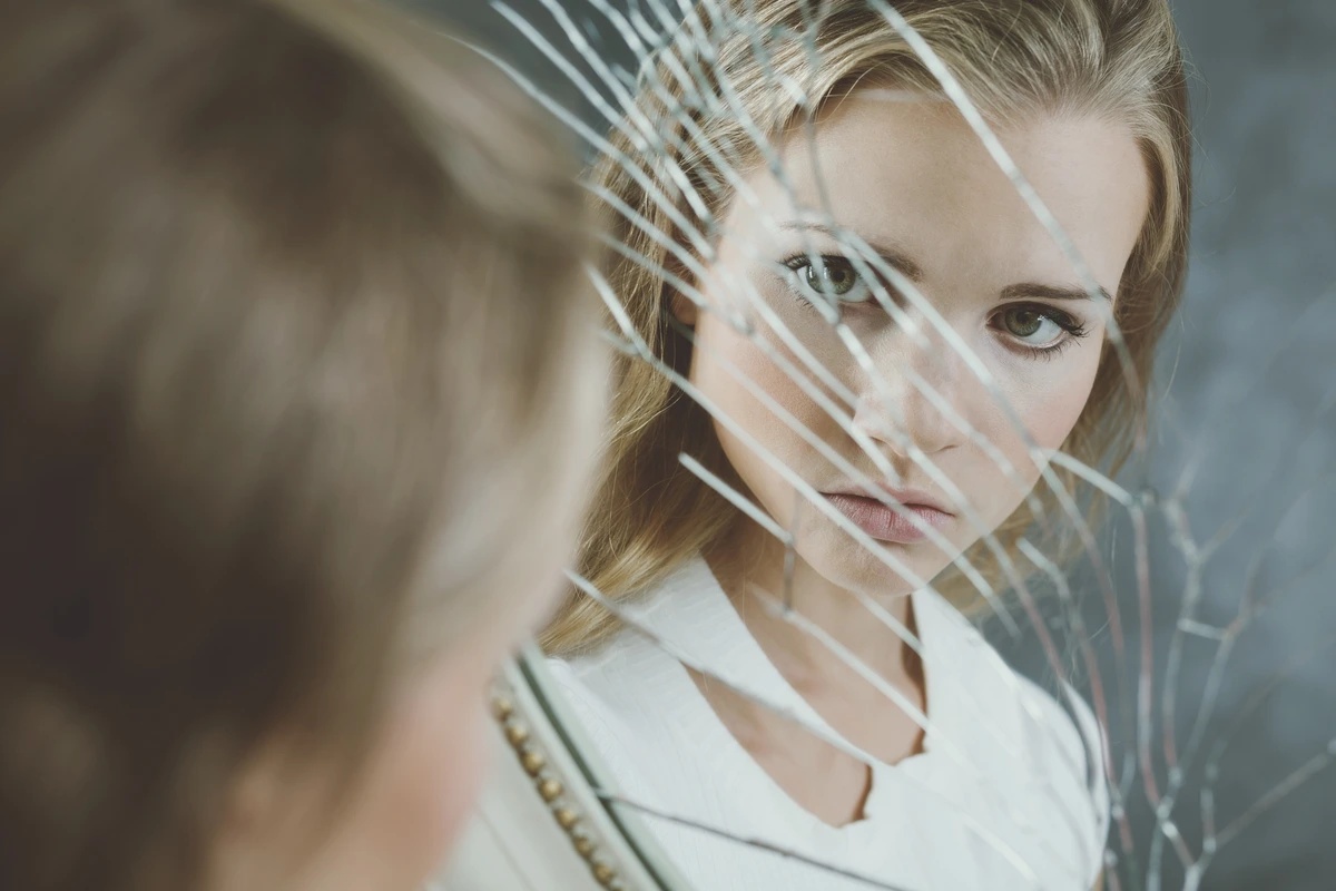 A woman with undifferentiated schizophrenia stares at her reflection in a broken mirror.