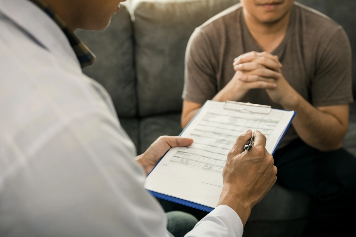 A doctor at an alcohol rehab takes notes on a clipboard while talking to his patient.