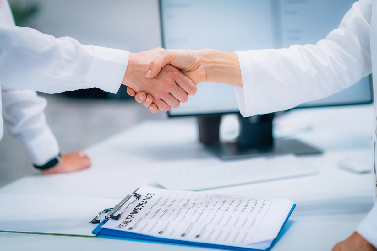 Two clinicians at an alcohol rehab shake hands over some clipboards and forms.