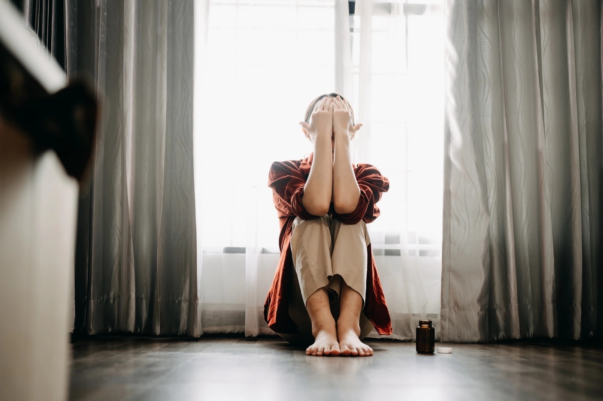 Woman sitting in front of a window with her face in her hands.