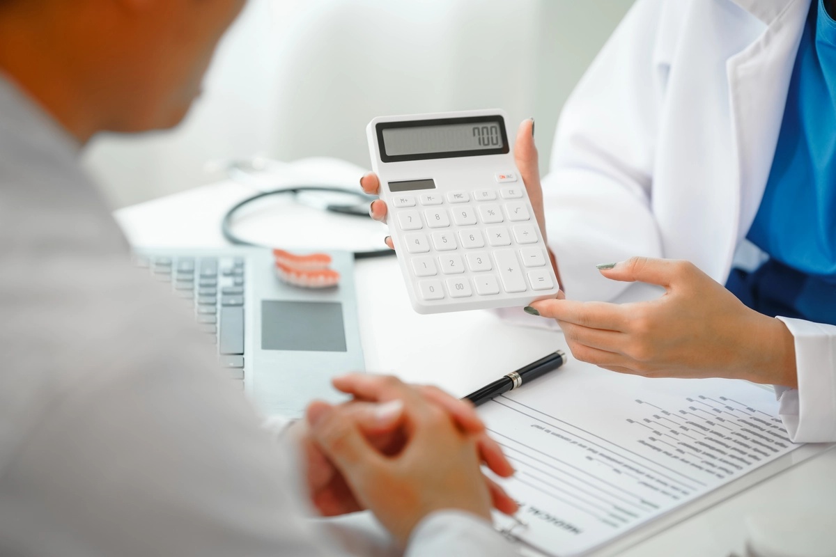 A doctor holds a calculator toward a drug rehab patient, explaining how much drug rehab costs.