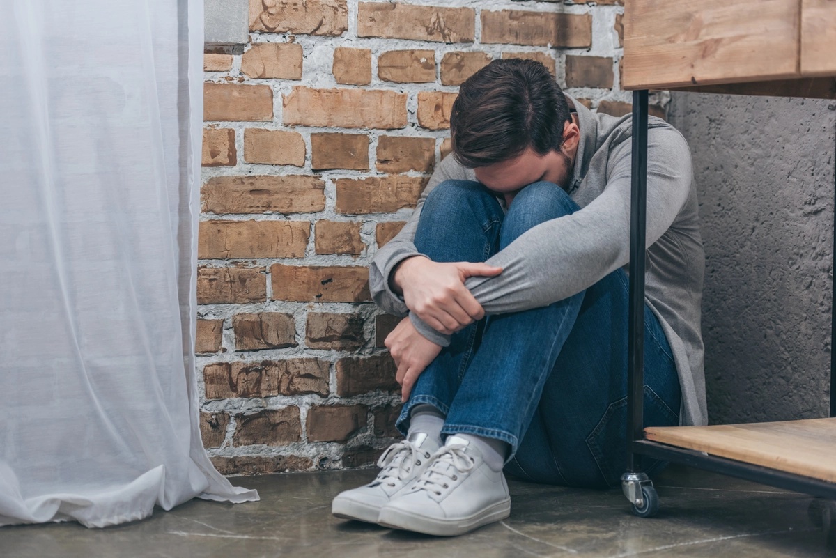 A man sitting in a corner in a curled position, likely suffering from symptoms of panic disorder.