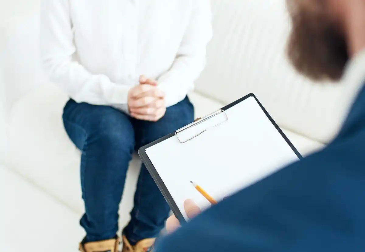 A therapist looks at his notes while his patient sits on a couch.