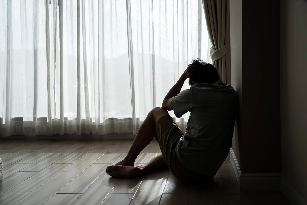 Man in a dark room leans against the wall while on the floor.