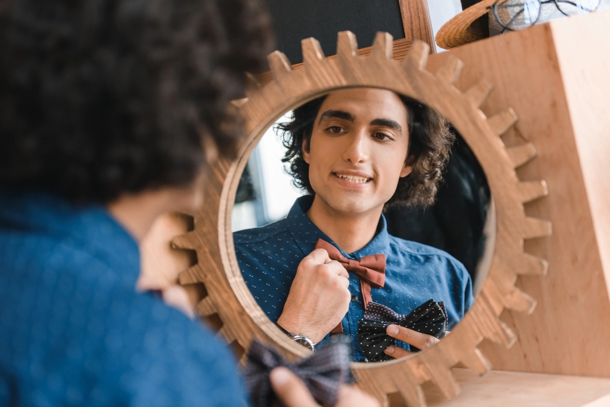 A man nervously adjusts his bow tie while looking in a mirror.