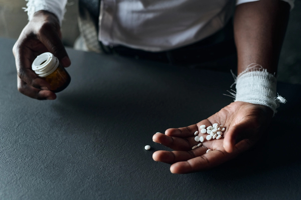 A man struggling with prescription drug addiction poses with pills and a pill bottle in his hands.