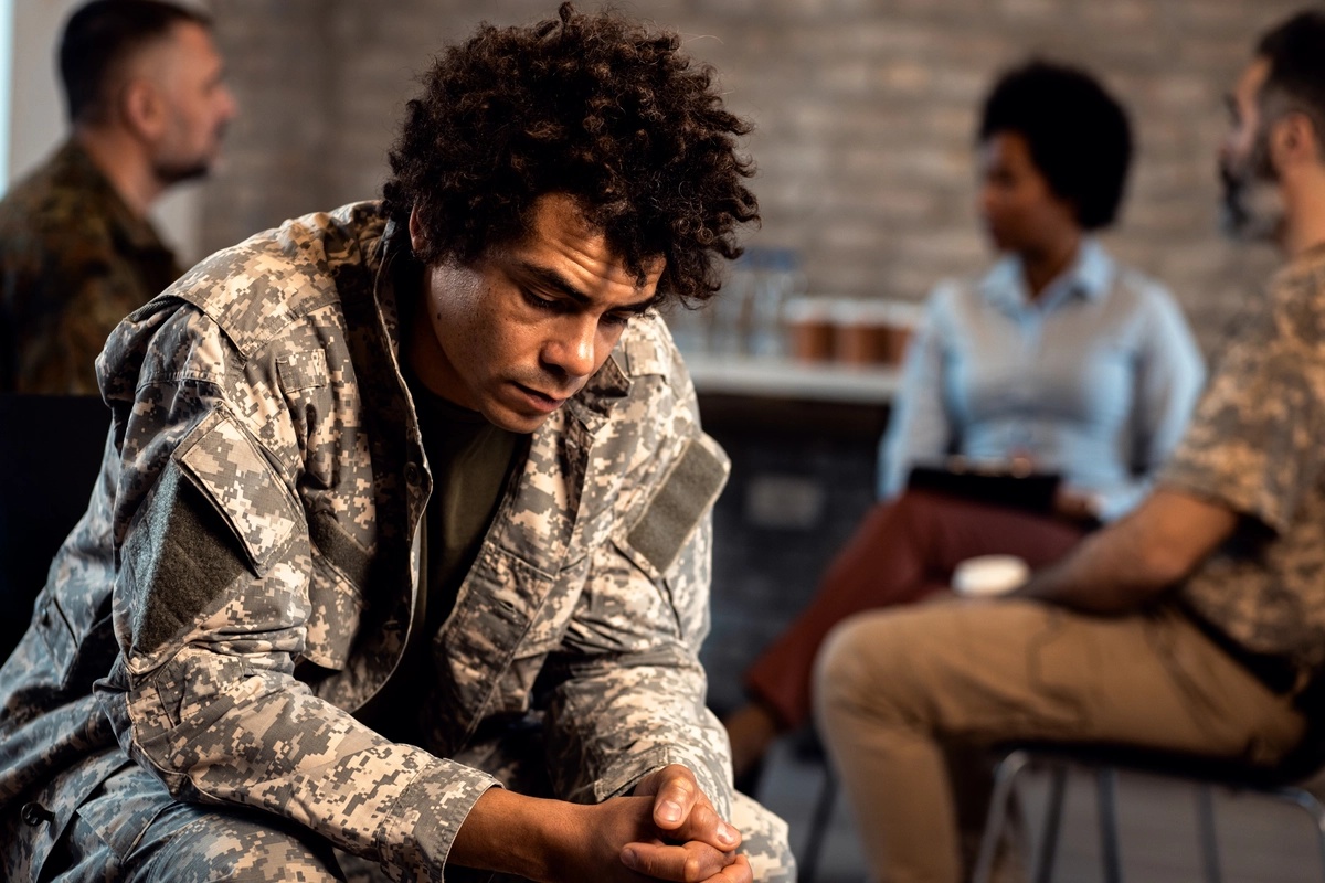 A man in outpatient care sitting at a group therapy session with his back to the group.