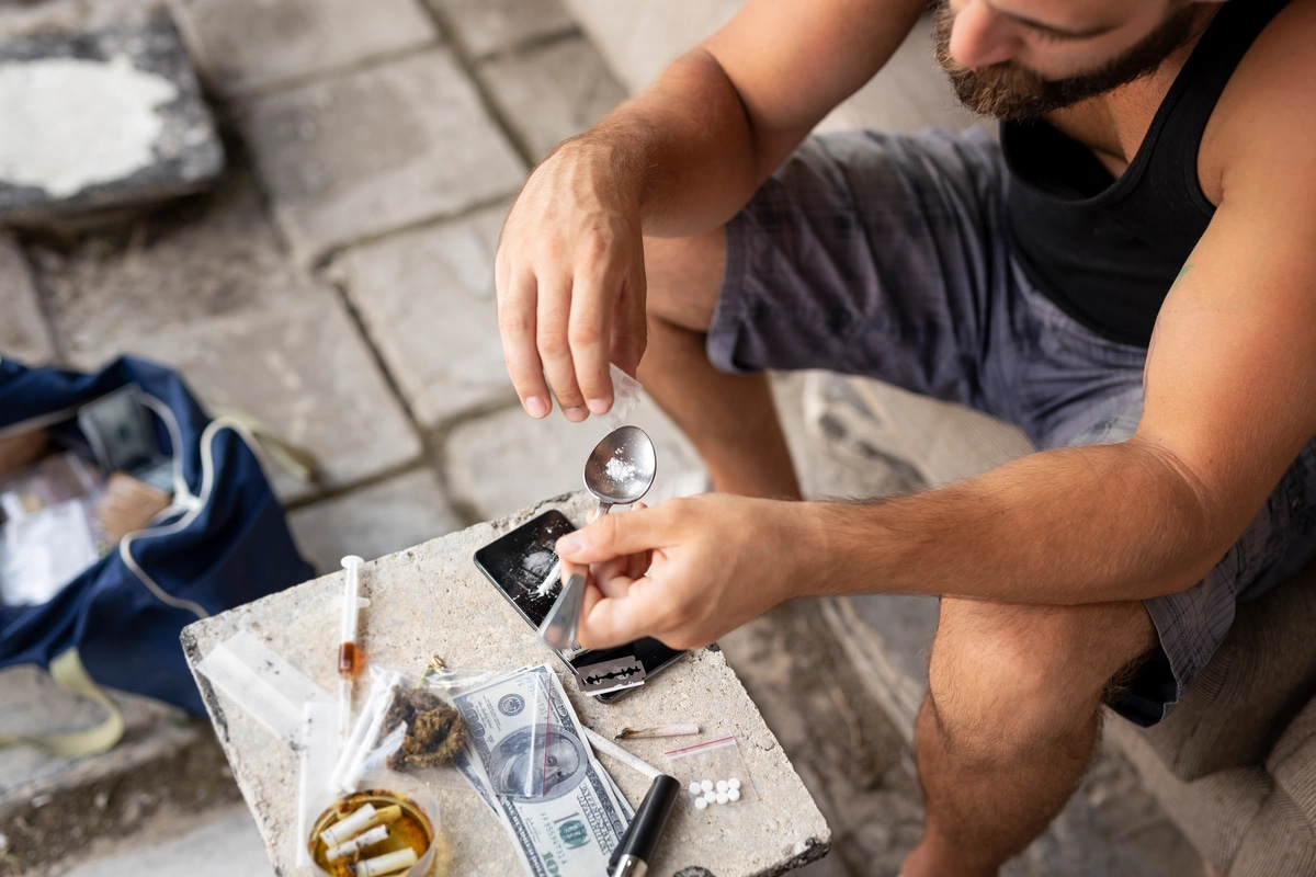 A man dealing with meth addiction sits in front of a table with drug paraphernalia on it.