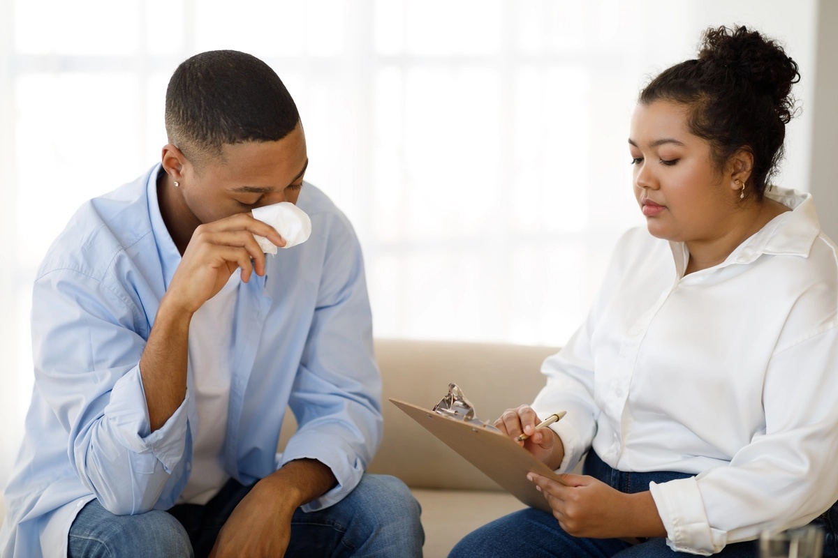 A man crying with tissues as an alumni support group leader tends to his struggles.