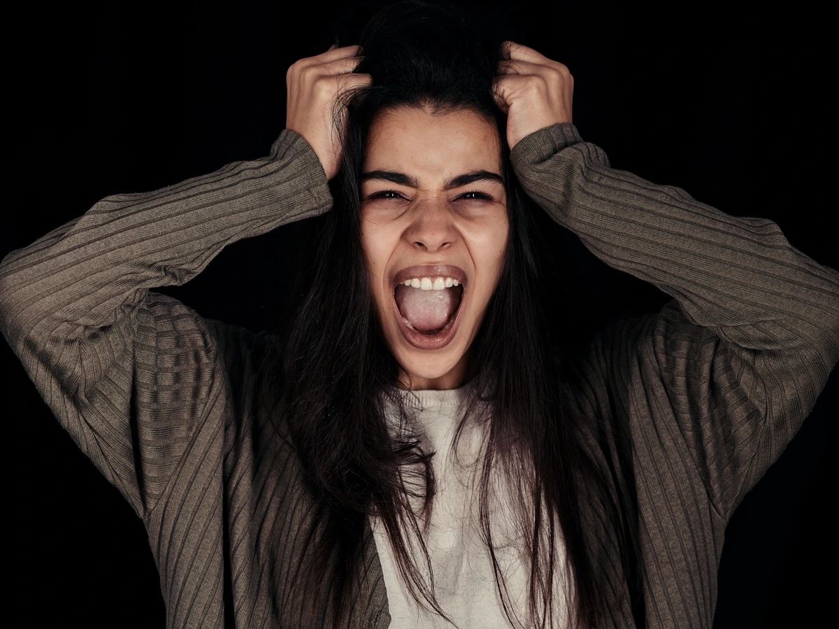 A woman with her hands to her head. She seems to be screaming.