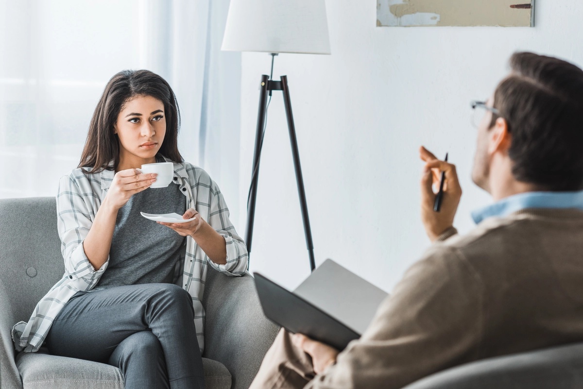 Woman sips coffee or tea while talking to her therapist.