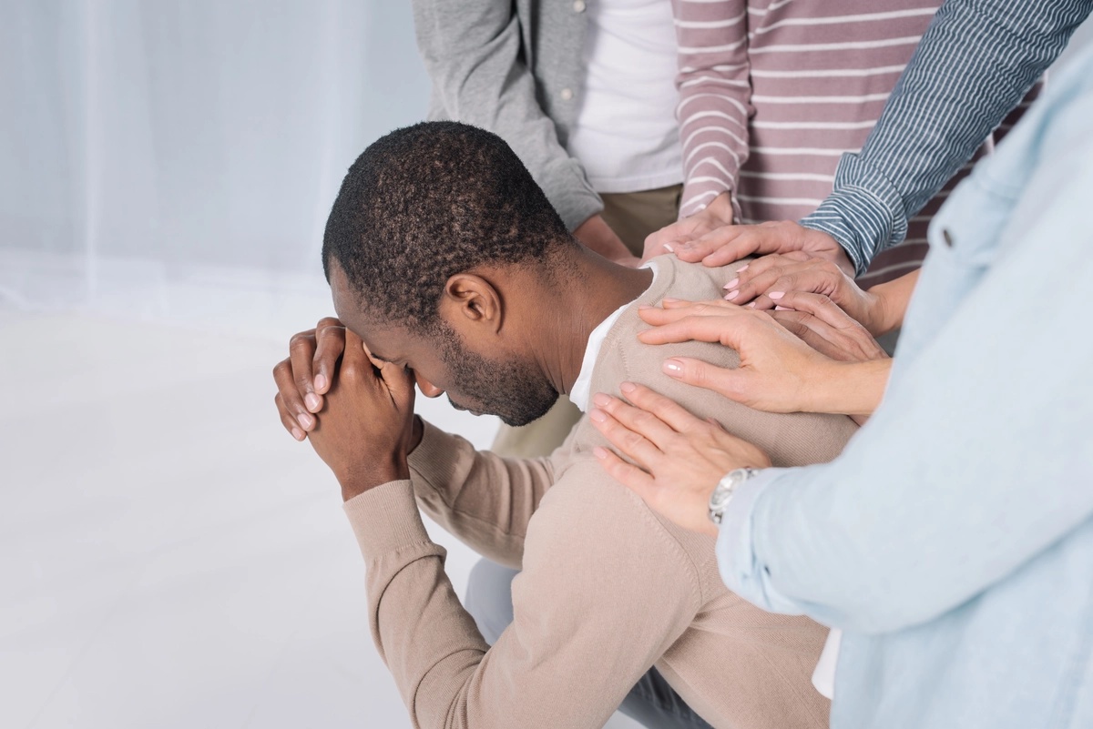 A man holding his hands to his head in a sad manner, and being comforted by members of his alumni support group.