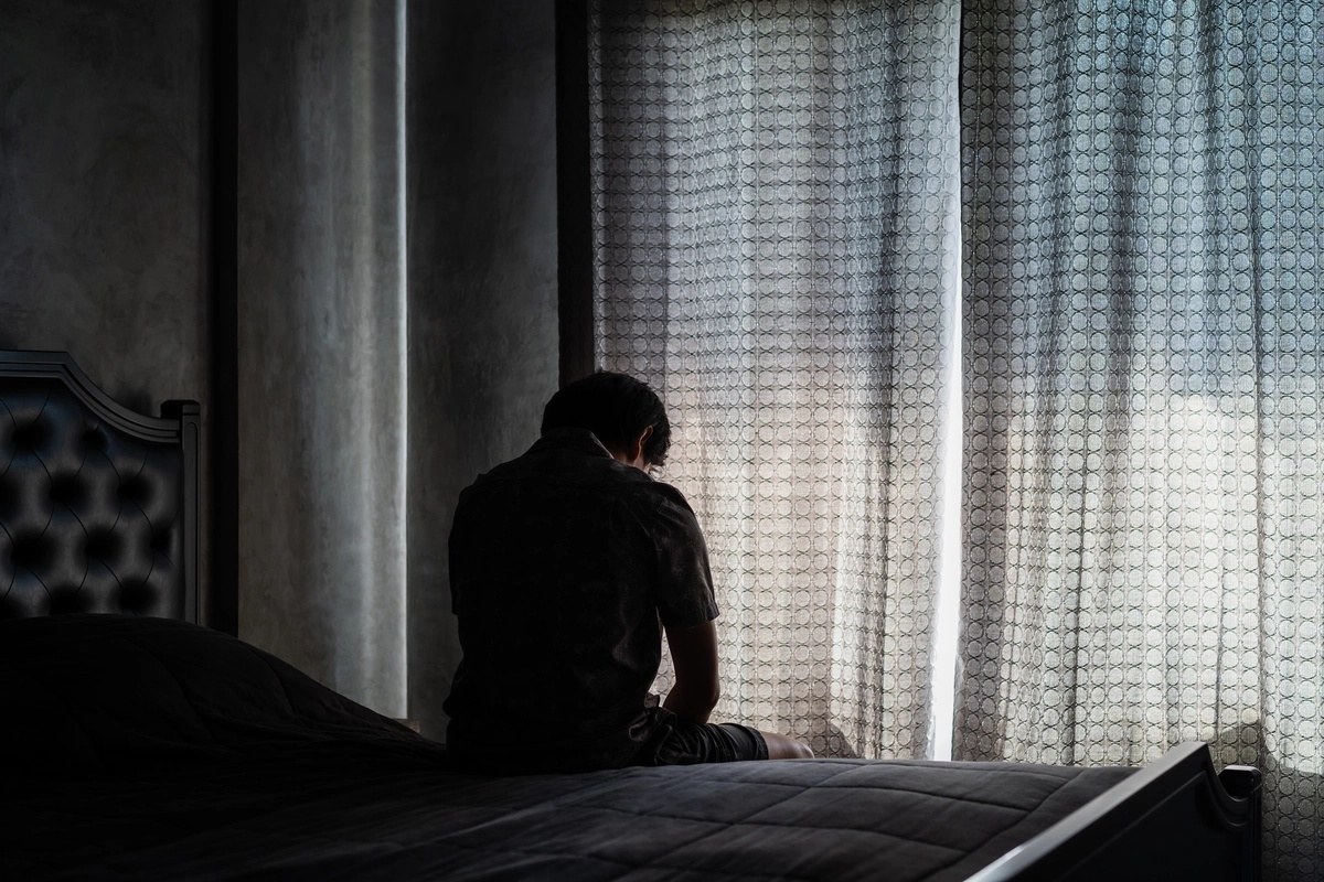 A person sitting on the end of their bed in a slouched manner, struggling with symptoms of GAD.