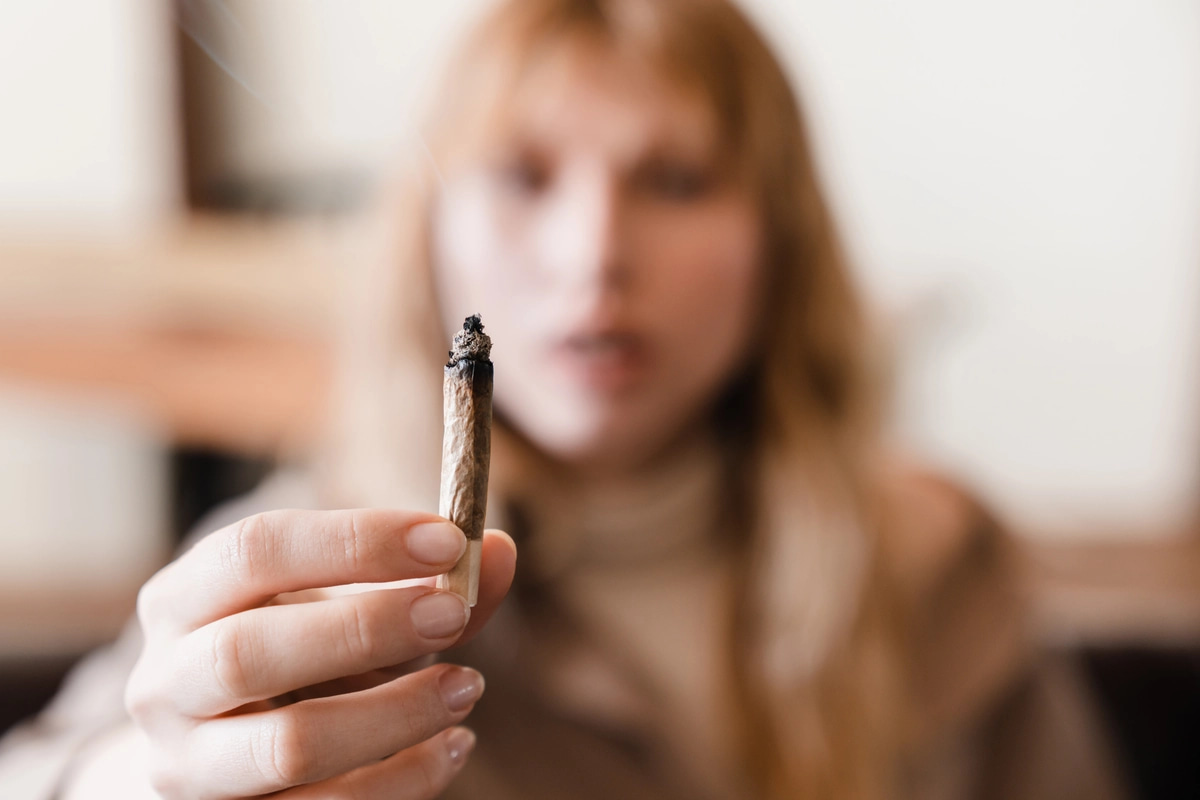 A woman with marijuana addiction holds a joint up to the camera.