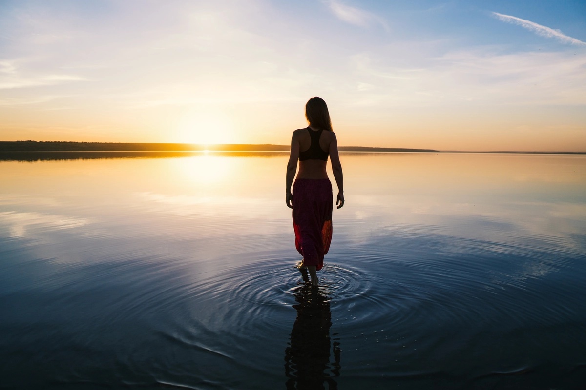 A woman experiencing the clarity and benefits of individual therapy while walking on a lake toward the sunset.