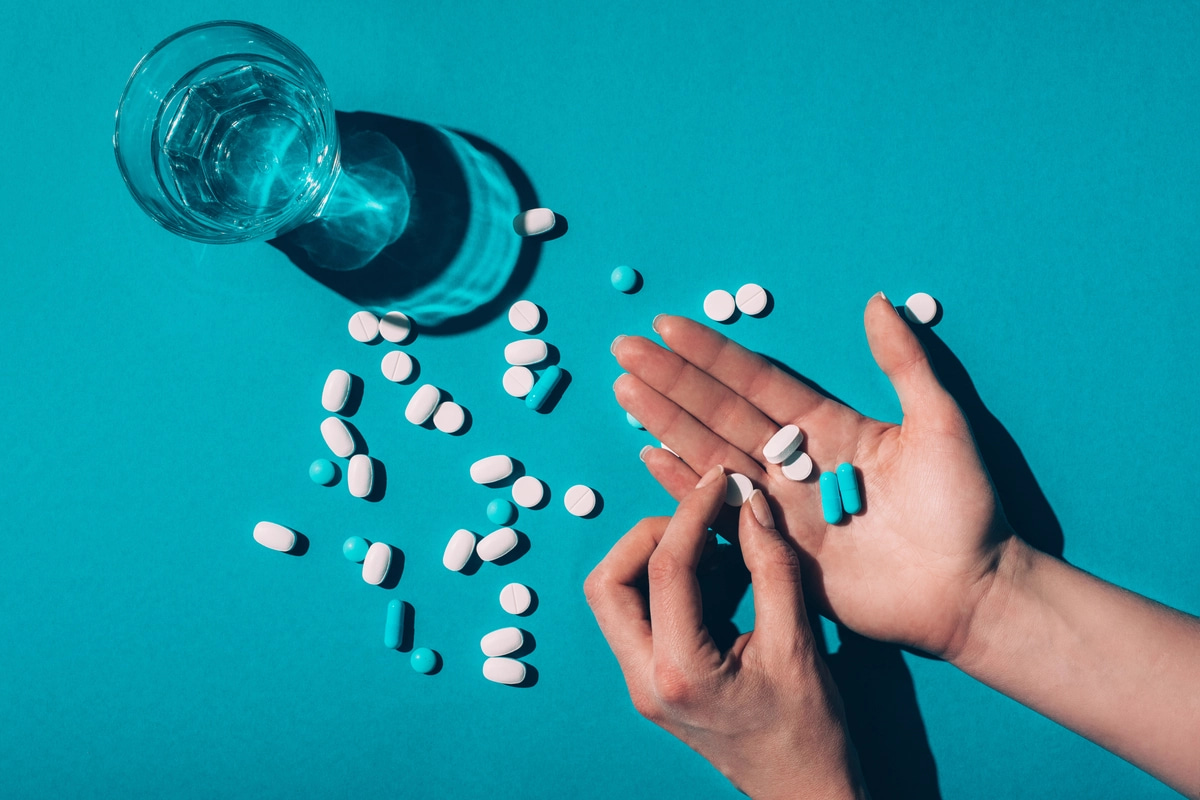 A person holds pills, with more pills and a glass of water on a table, a sign of opioid addiction.