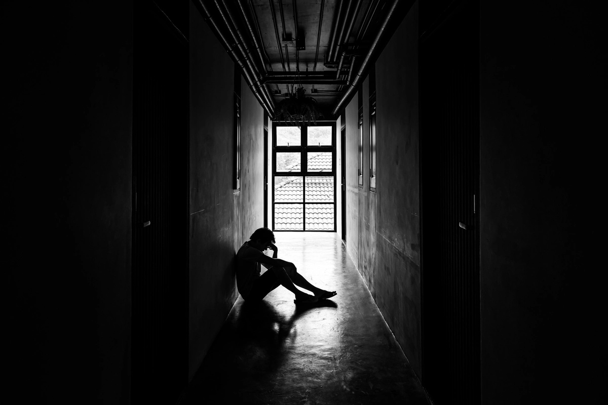 A person sits against a wall in a dark hallway.