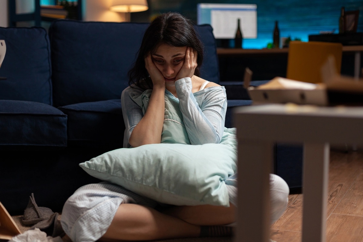 A woman sitting cross-legged in front of her couch with her head in her hands