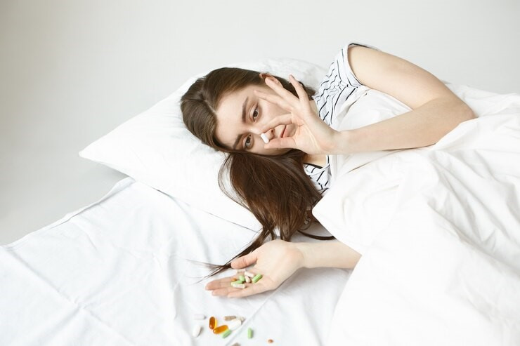 Woman in bed near pills. She's also holding pills.