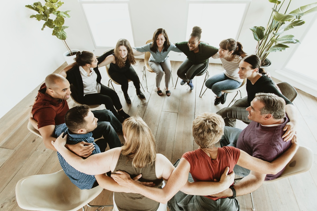 A group therapy session at alcohol rehab, with people placing their arms on their partners' backs.