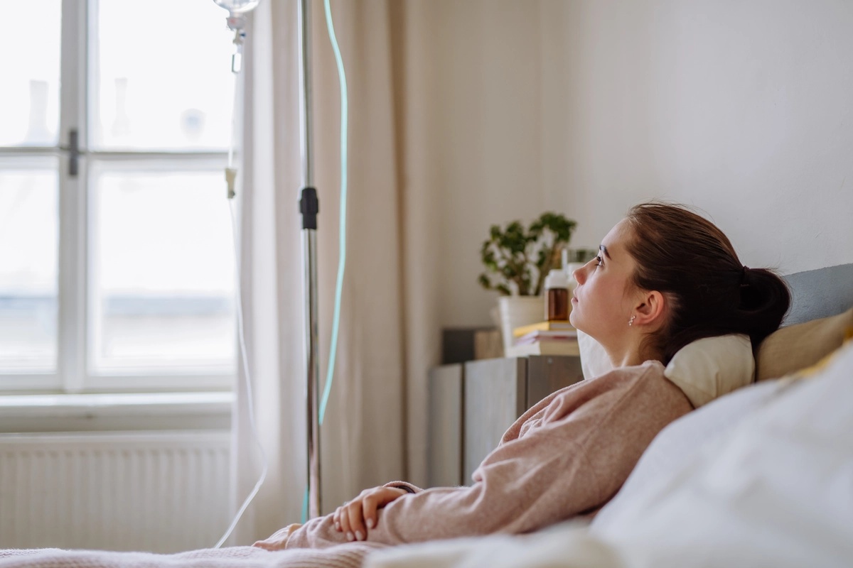 A woman resting on a bed with an IV line after going through drug detox.