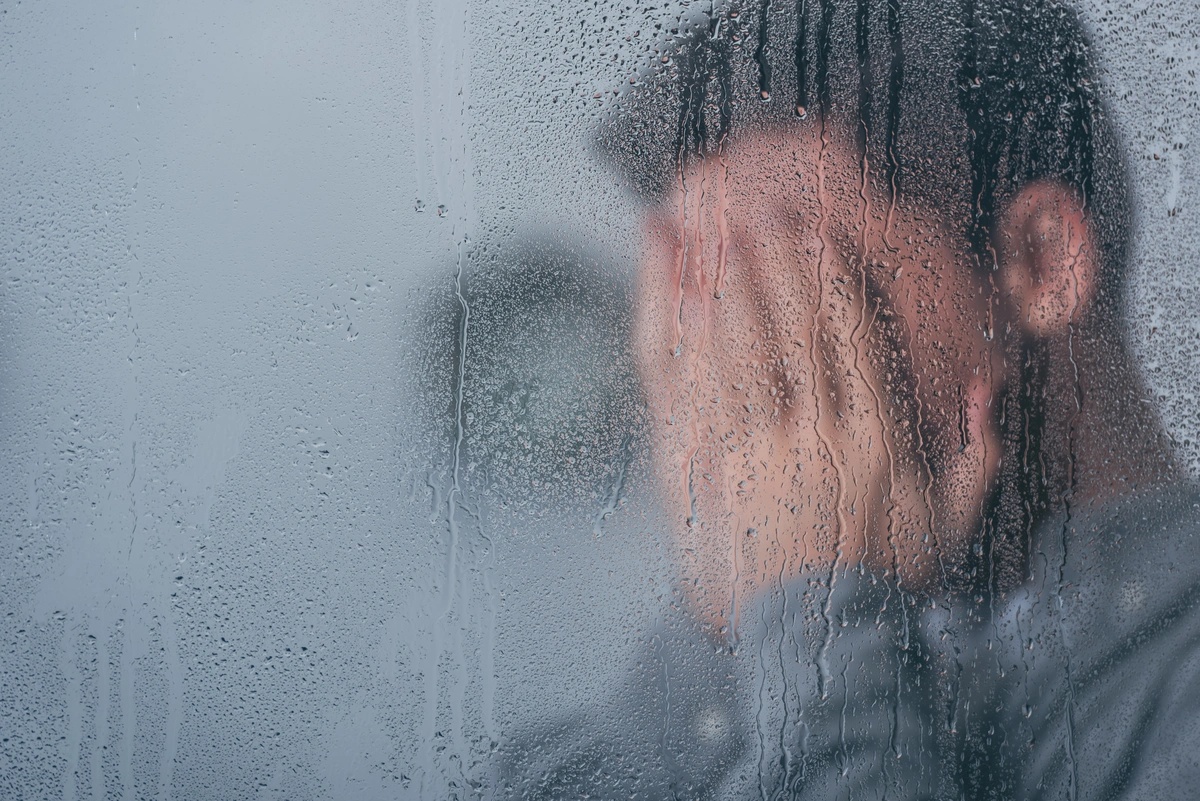 A man holding his hands to his face behind a wet window.