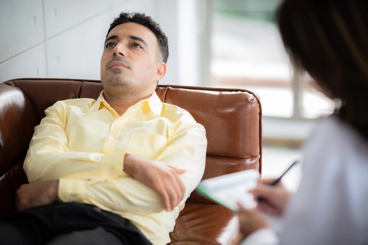 A man lying on a therapist's couch while the therapist takes notes.