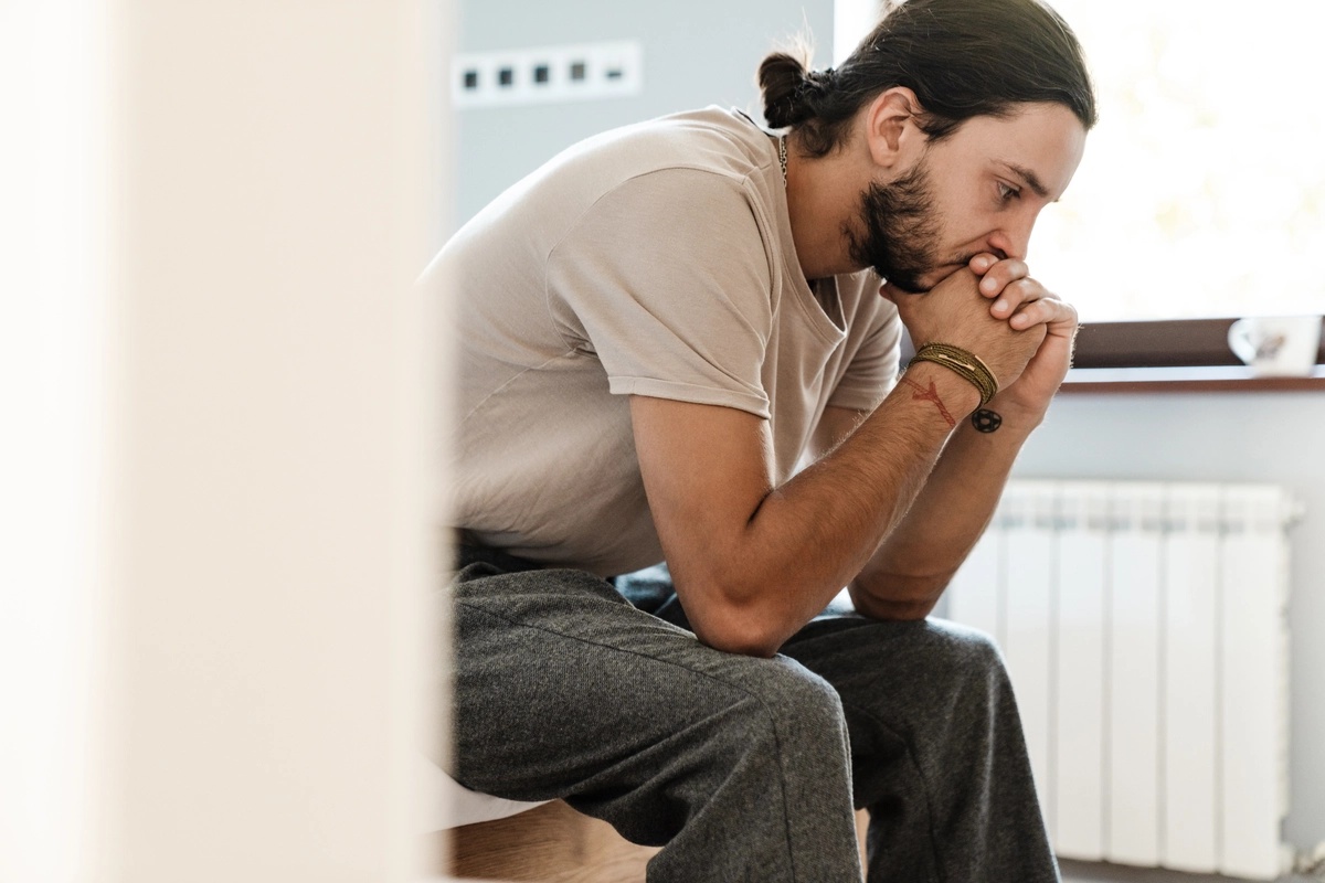 A man sitting on the corner of his bed and struggling with symptoms of major depressive disorder.