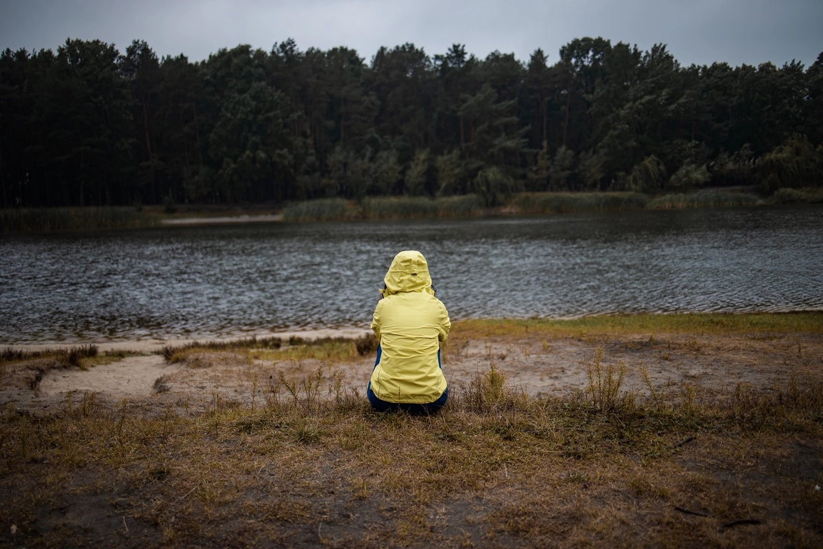 A person sitting by themselves in front of a river or a lake.