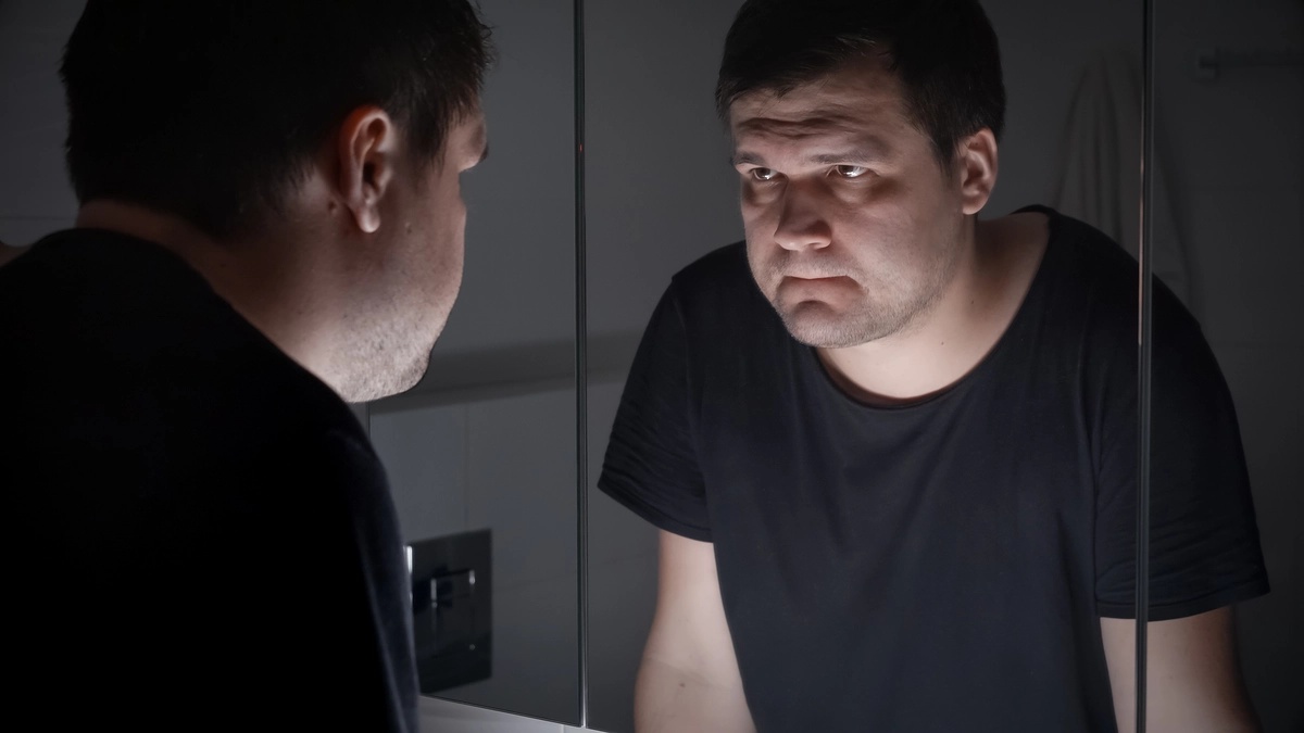 A man staring at himself in a mirror wondering about the causes of simple schizophrenia.