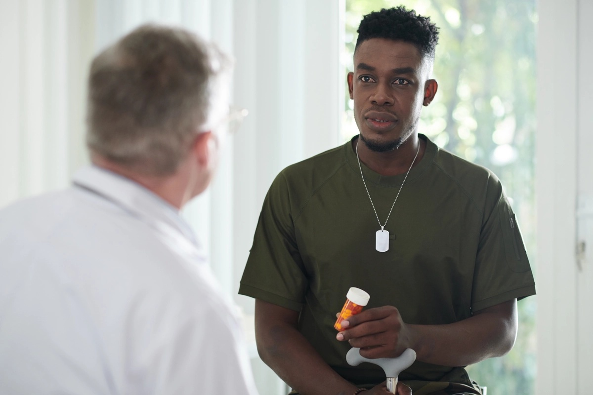 A  man holding a pill bottle talks with his doctor.