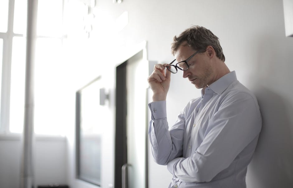Photo of a man learning aginst a wall taking his glasses off.