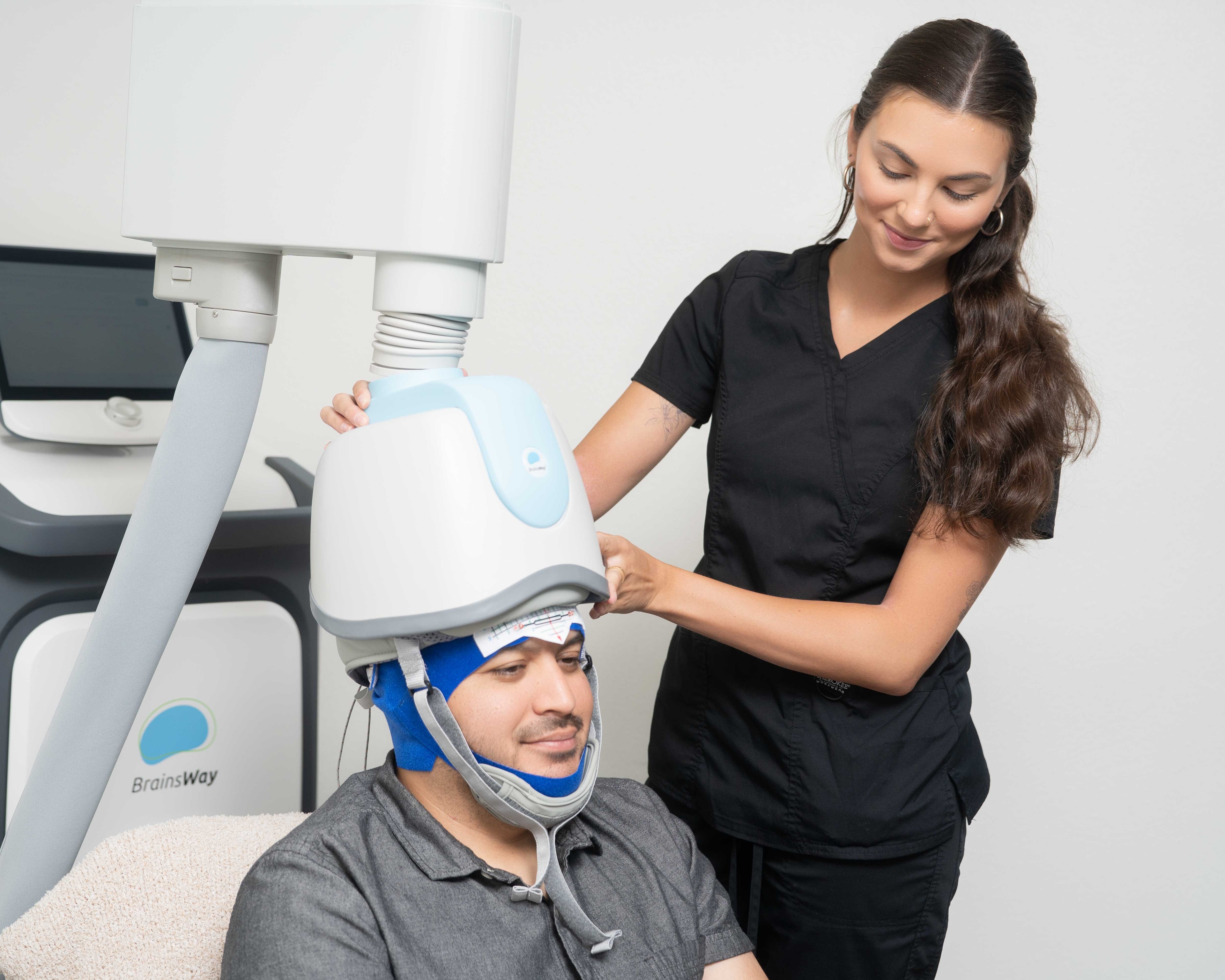 TMS: A man wearing a TMS device being adjusted by a TMS professional.