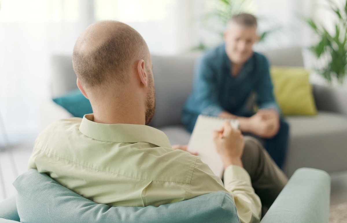 A therapist talks to his patient on a couch.