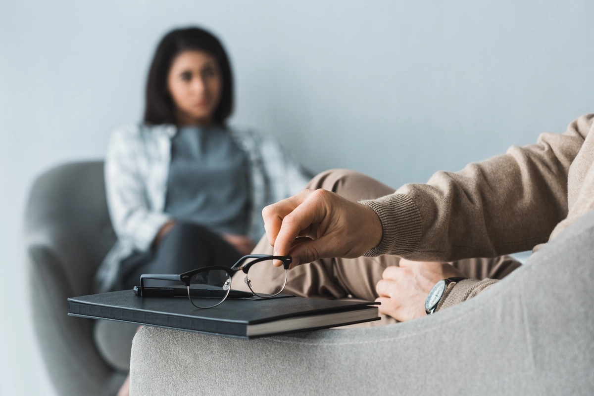 A therapist placing their glasses on a notebook during an individual therapy session with a patient.