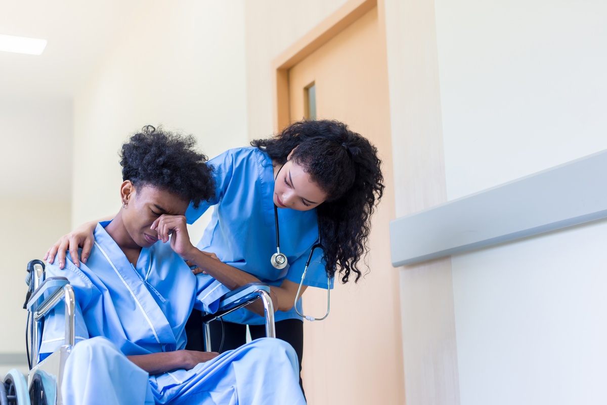 A sad man in a wheelchair in inpatient care, being comforted by a doctor.