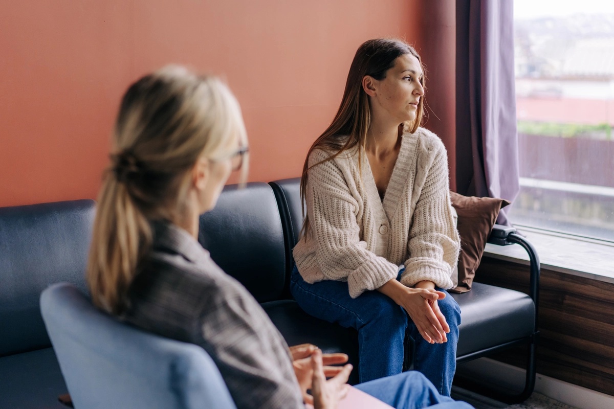 A therapist talks with her patient on a couch about treatment options, such as outpatient rehab.