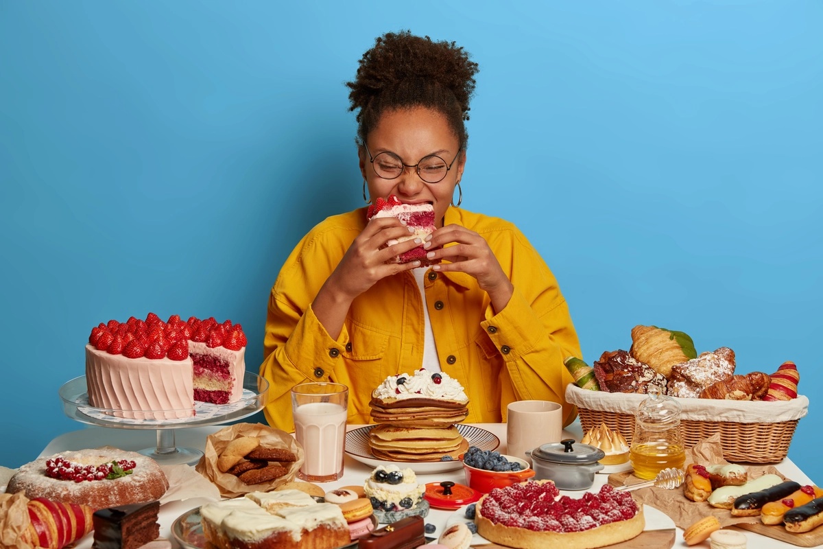 A woman, potentially with a food addiction, eating a large platter of desserts.