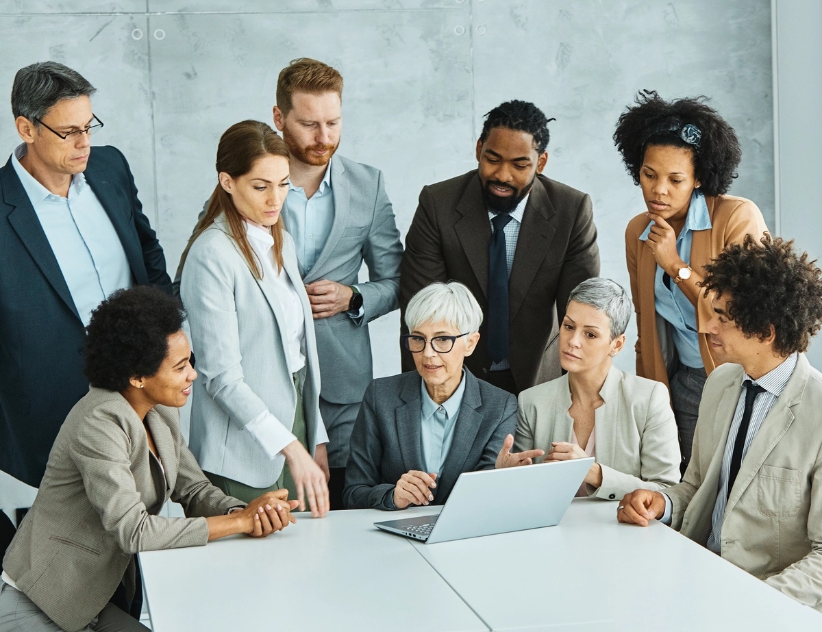 A group of case managers gathered around a woman with a laptop at a table.