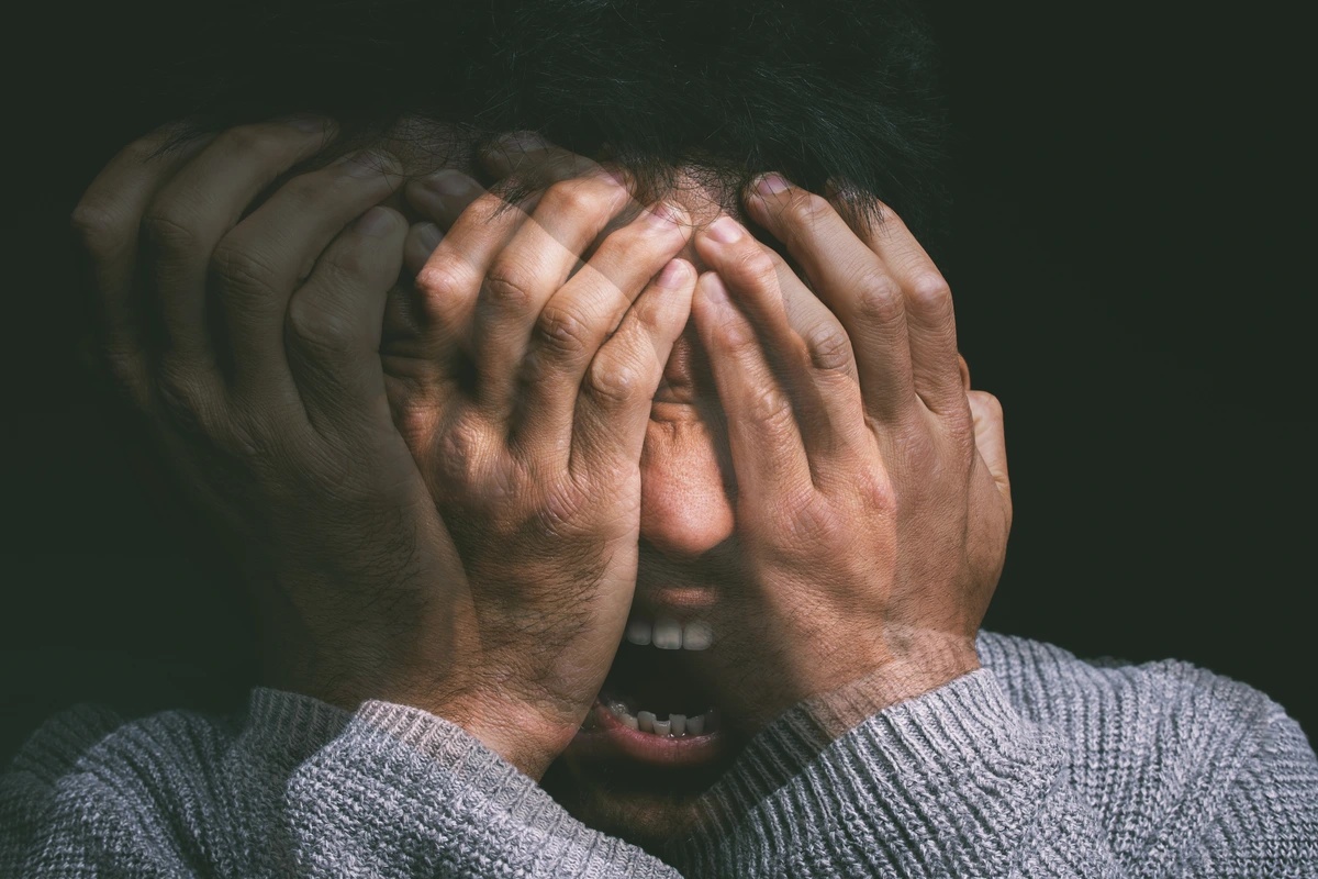 A blurry picture of a man suffering from simple schizophrenia holding his hands to his face with his mouth open frustrated and scared.