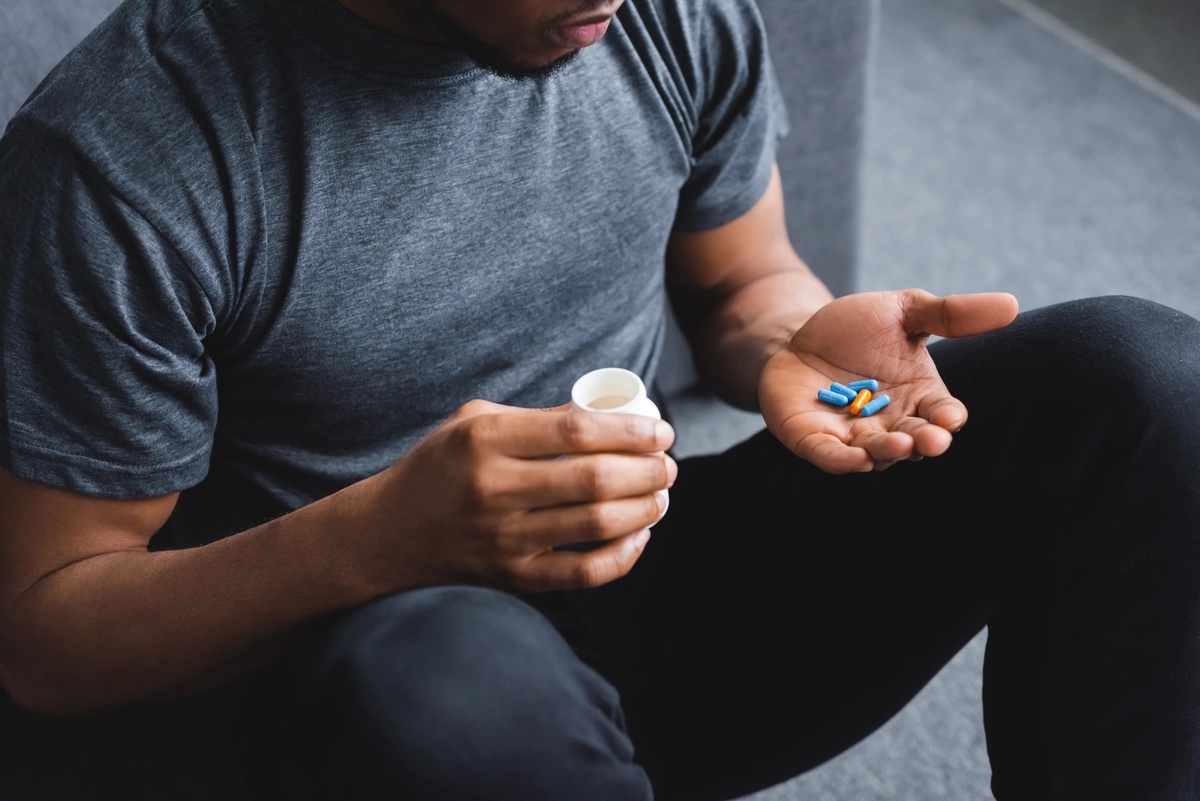 A man sitting down and holding a handful of stimulants in his hand, possibly struggling with stimulant addiction.