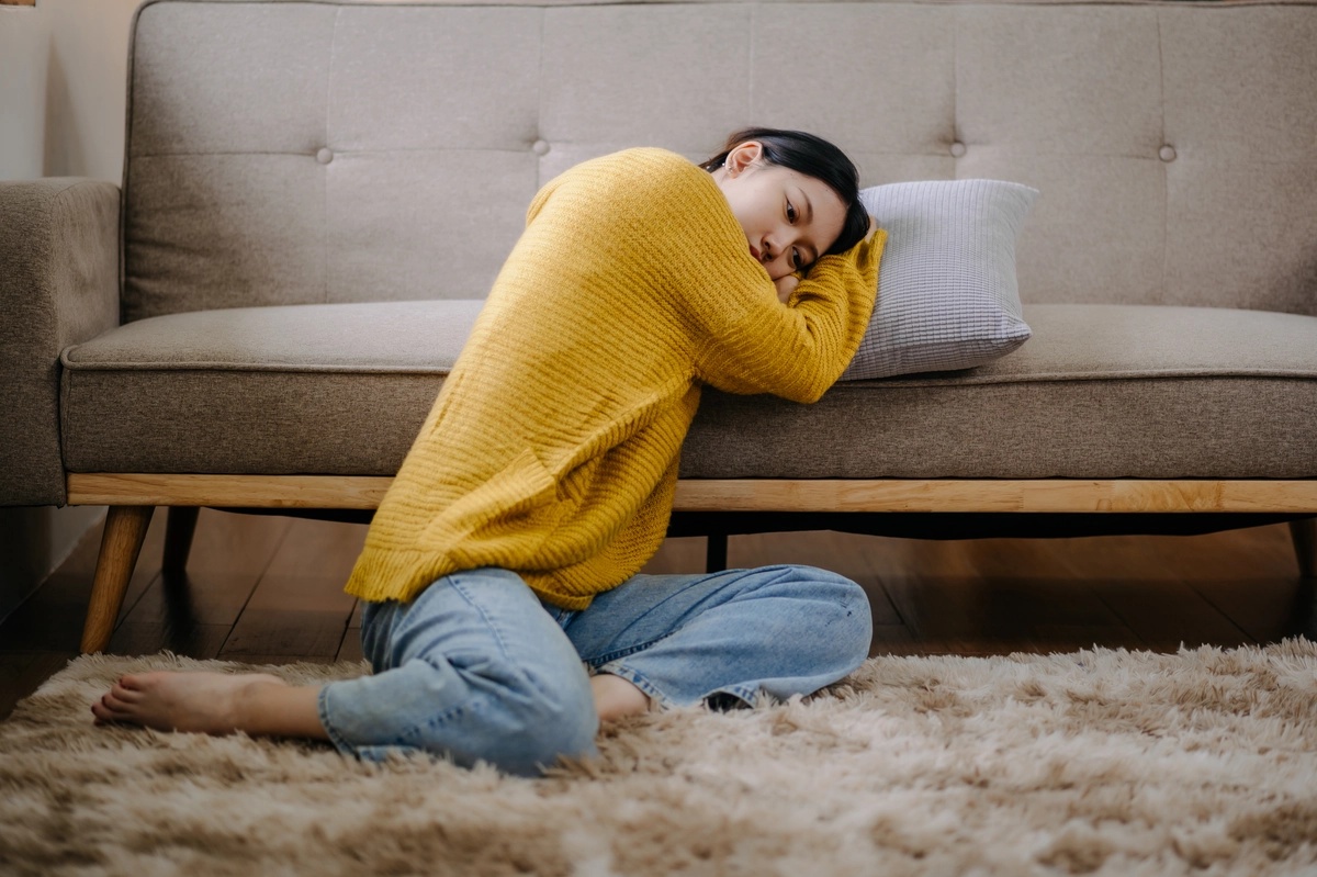 A woman with her head on a pillow by a couch.