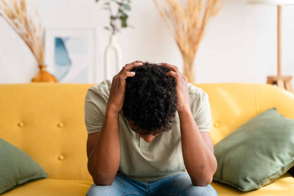 A man sitting on the couch with his hands on his head.