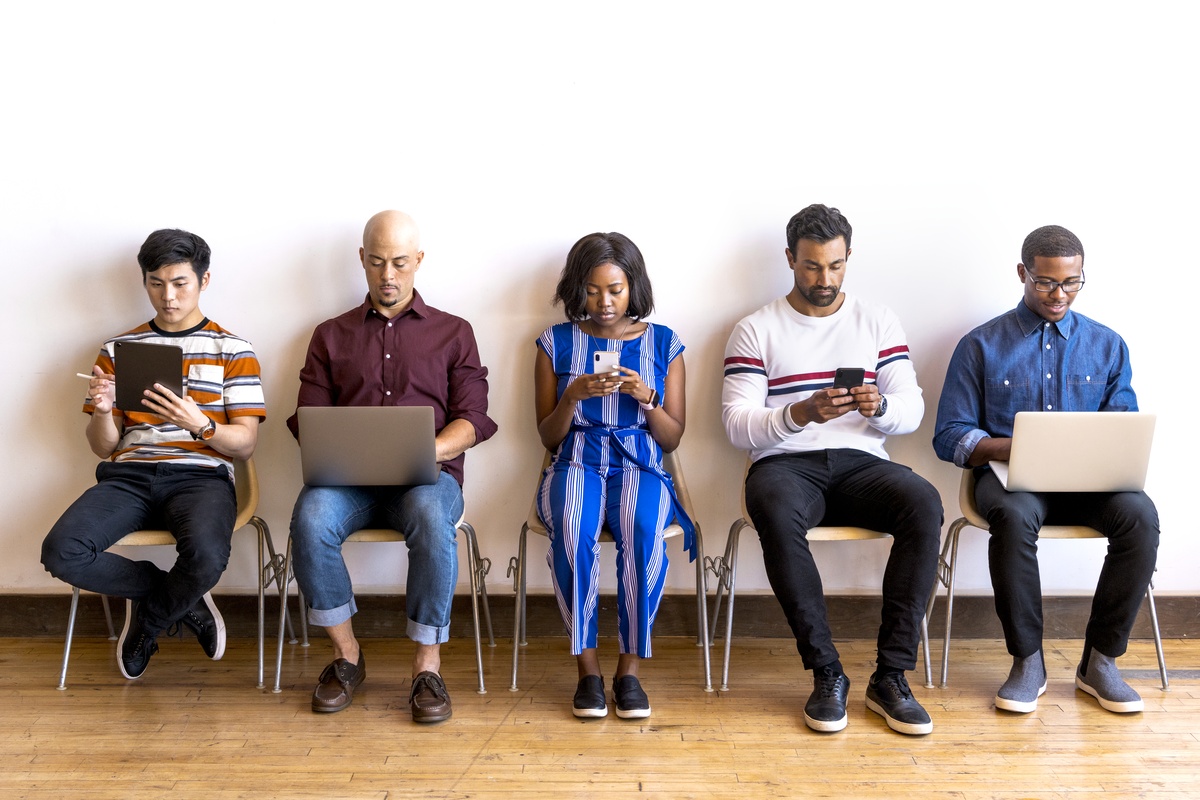 A group of five people all staring at their mobile devices and laptops due to internet addiction.