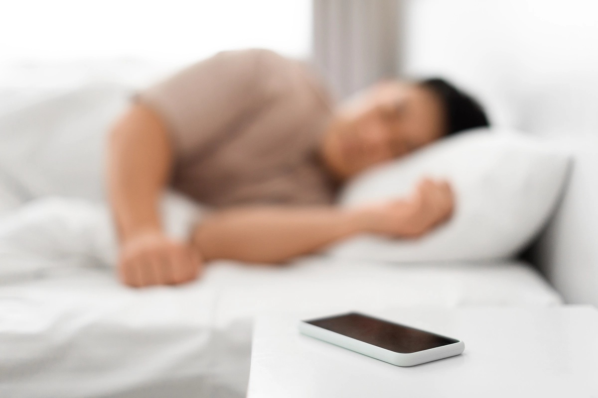 A person sleeping with their phone sitting on the nightstand, possibly suffering from a phone addiction.